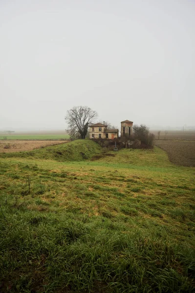 Bir tarlada terk edilmiş bir baraj, yanında çıplak bir ağaç olan bir hendek, İtalya 'nın kışın kırsalında sisli ve bulutlu bir günde.