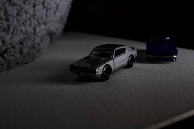 Mantova, İtalya - 3RD JANUARY 2025 Takara Tomy kopyaları gri Nissan Skyline 2000 GT-R ve mavi Nissan Fairlady Z beyaz bir panoda, gri bir kumaş parçasının yanında, uçurumun kenarındaki bir dağ yolunda yarış yapıyormuş gibi yapıyor.