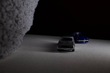 Mantova, İtalya - 3RD JANUARY 2025 Takara Tomy kopyaları gri Nissan Skyline 2000 GT-R ve mavi Nissan Fairlady Z beyaz bir panoda, gri bir kumaş parçasının yanında, uçurumun kenarındaki bir dağ yolunda yarış yapıyormuş gibi yapıyor.