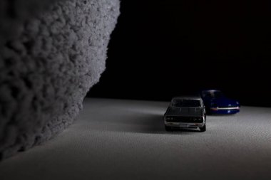 Mantova, İtalya - 3RD JANUARY 2025 Takara Tomy kopyaları gri Nissan Skyline 2000 GT-R ve mavi Nissan Fairlady Z beyaz bir panoda, gri bir kumaş parçasının yanında, uçurumun kenarındaki bir dağ yolunda yarış yapıyormuş gibi yapıyor.