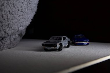 Mantova, İtalya - 3RD JANUARY 2025 Takara Tomy kopyaları gri Nissan Skyline 2000 GT-R ve mavi Nissan Fairlady Z beyaz bir panoda, gri bir kumaş parçasının yanında, uçurumun kenarındaki bir dağ yolunda yarış yapıyormuş gibi yapıyor.