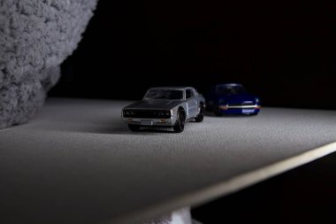 Mantova, İtalya - 3RD JANUARY 2025 Takara Tomy kopyaları gri Nissan Skyline 2000 GT-R ve mavi Nissan Fairlady Z beyaz bir panoda, gri bir kumaş parçasının yanında, uçurumun kenarındaki bir dağ yolunda yarış yapıyormuş gibi yapıyor.