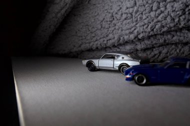 Mantova, İtalya - 3RD JANUARY 2025 Takara Tomy kopyaları gri Nissan Skyline 2000 GT-R ve mavi Nissan Fairlady Z beyaz bir panoda, gri bir kumaş parçasının yanında, uçurumun kenarındaki bir dağ yolunda yarış yapıyormuş gibi yapıyor.