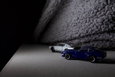 Mantova, İtalya - 3RD JANUARY 2025 Takara Tomy kopyaları gri Nissan Skyline 2000 GT-R ve mavi Nissan Fairlady Z beyaz bir panoda, gri bir kumaş parçasının yanında, uçurumun kenarındaki bir dağ yolunda yarış yapıyormuş gibi yapıyor.