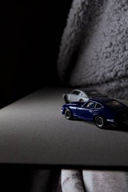 Mantova, İtalya - 3RD JANUARY 2025 Takara Tomy kopyaları gri Nissan Skyline 2000 GT-R ve mavi Nissan Fairlady Z beyaz bir panoda, gri bir kumaş parçasının yanında, uçurumun kenarındaki bir dağ yolunda yarış yapıyormuş gibi yapıyor.