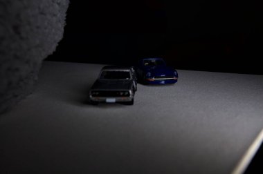 Mantova, İtalya - 3RD JANUARY 2025 Takara Tomy kopyaları gri Nissan Skyline 2000 GT-R ve mavi Nissan Fairlady Z beyaz bir panoda, gri bir kumaş parçasının yanında, uçurumun kenarındaki bir dağ yolunda yarış yapıyormuş gibi yapıyor.