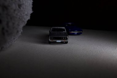 Mantova, İtalya - 3RD JANUARY 2025 Takara Tomy kopyaları gri Nissan Skyline 2000 GT-R ve mavi Nissan Fairlady Z beyaz bir panoda, gri bir kumaş parçasının yanında, uçurumun kenarındaki bir dağ yolunda yarış yapıyormuş gibi yapıyor.