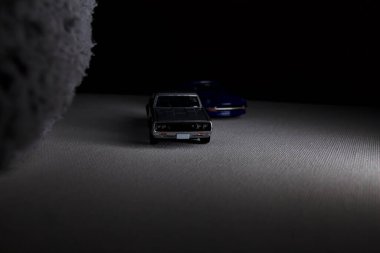 Mantova, İtalya - 3RD JANUARY 2025 Takara Tomy kopyaları gri Nissan Skyline 2000 GT-R ve mavi Nissan Fairlady Z beyaz bir panoda, gri bir kumaş parçasının yanında, uçurumun kenarındaki bir dağ yolunda yarış yapıyormuş gibi yapıyor.