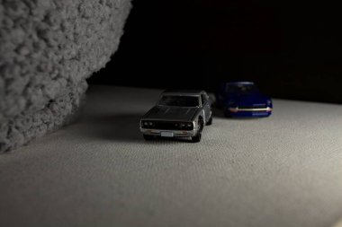 Mantova, İtalya - 3RD JANUARY 2025 Takara Tomy kopyaları gri Nissan Skyline 2000 GT-R ve mavi Nissan Fairlady Z beyaz bir panoda, gri bir kumaş parçasının yanında, uçurumun kenarındaki bir dağ yolunda yarış yapıyormuş gibi yapıyor.