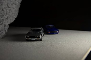 Mantova, İtalya - 3RD JANUARY 2025 Takara Tomy kopyaları gri Nissan Skyline 2000 GT-R ve mavi Nissan Fairlady Z beyaz bir panoda, gri bir kumaş parçasının yanında, uçurumun kenarındaki bir dağ yolunda yarış yapıyormuş gibi yapıyor.