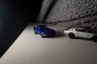 Mantova, İtalya - 3RD JANUARY 2025 Takara Tomy kopyaları gri Nissan Skyline 2000 GT-R ve mavi Nissan Fairlady Z beyaz bir panoda, gri bir kumaş parçasının yanında, uçurumun kenarındaki bir dağ yolunda yarış yapıyormuş gibi yapıyor.