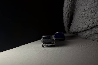 Mantova, İtalya - 3RD JANUARY 2025 Takara Tomy kopyaları gri Nissan Skyline 2000 GT-R ve mavi Nissan Fairlady Z beyaz bir panoda, gri bir kumaş parçasının yanında, uçurumun kenarındaki bir dağ yolunda yarış yapıyormuş gibi yapıyor.