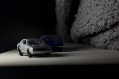 Mantova, İtalya - 3RD JANUARY 2025 Takara Tomy kopyaları gri Nissan Skyline 2000 GT-R ve mavi Nissan Fairlady Z beyaz bir panoda, gri bir kumaş parçasının yanında, uçurumun kenarındaki bir dağ yolunda yarış yapıyormuş gibi yapıyor.