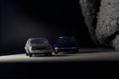 Mantova, İtalya - 3RD JANUARY 2025 Takara Tomy kopyaları gri Nissan Skyline 2000 GT-R ve mavi Nissan Fairlady Z beyaz bir panoda, gri bir kumaş parçasının yanında, uçurumun kenarındaki bir dağ yolunda yarış yapıyormuş gibi yapıyor.