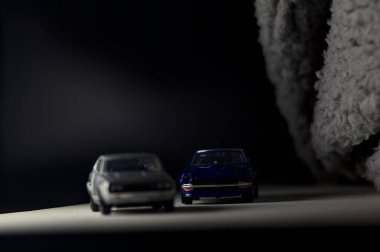 Mantova, İtalya - 3RD JANUARY 2025 Takara Tomy kopyaları gri Nissan Skyline 2000 GT-R ve mavi Nissan Fairlady Z beyaz bir panoda, gri bir kumaş parçasının yanında, uçurumun kenarındaki bir dağ yolunda yarış yapıyormuş gibi yapıyor.