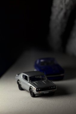 Mantova, İtalya - 3RD JANUARY 2025 Takara Tomy kopyaları gri Nissan Skyline 2000 GT-R ve mavi Nissan Fairlady Z beyaz bir panoda, gri bir kumaş parçasının yanında, uçurumun kenarındaki bir dağ yolunda yarış yapıyormuş gibi yapıyor.