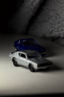 Mantova, İtalya - 3RD JANUARY 2025 Takara Tomy kopyaları gri Nissan Skyline 2000 GT-R ve mavi Nissan Fairlady Z beyaz bir panoda, gri bir kumaş parçasının yanında, uçurumun kenarındaki bir dağ yolunda yarış yapıyormuş gibi yapıyor.