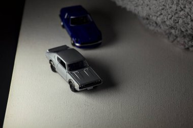 Mantova, İtalya - 3RD JANUARY 2025 Takara Tomy kopyaları gri Nissan Skyline 2000 GT-R ve mavi Nissan Fairlady Z beyaz bir panoda, gri bir kumaş parçasının yanında, uçurumun kenarındaki bir dağ yolunda yarış yapıyormuş gibi yapıyor.