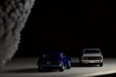 Mantova, İtalya - 3RD JANUARY 2025 Takara Tomy kopyaları gri Nissan Skyline 2000 GT-R ve mavi Nissan Fairlady Z beyaz bir panoda, gri bir kumaş parçasının yanında, uçurumun kenarındaki bir dağ yolunda yarış yapıyormuş gibi yapıyor.