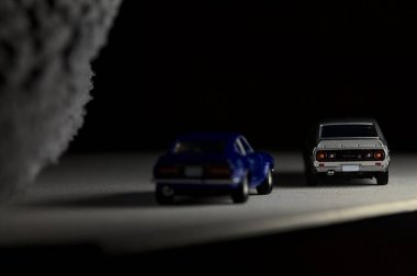 Mantova, İtalya - 3RD JANUARY 2025 Takara Tomy kopyaları gri Nissan Skyline 2000 GT-R ve mavi Nissan Fairlady Z beyaz bir panoda, gri bir kumaş parçasının yanında, uçurumun kenarındaki bir dağ yolunda yarış yapıyormuş gibi yapıyor.