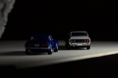 Mantova, İtalya - 3RD JANUARY 2025 Takara Tomy kopyaları gri Nissan Skyline 2000 GT-R ve mavi Nissan Fairlady Z beyaz bir panoda, gri bir kumaş parçasının yanında, uçurumun kenarındaki bir dağ yolunda yarış yapıyormuş gibi yapıyor.