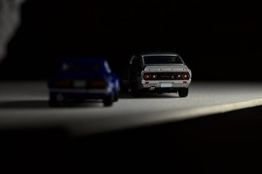 Mantova, İtalya - 3RD JANUARY 2025 Takara Tomy kopyaları gri Nissan Skyline 2000 GT-R ve mavi Nissan Fairlady Z beyaz bir panoda, gri bir kumaş parçasının yanında, uçurumun kenarındaki bir dağ yolunda yarış yapıyormuş gibi yapıyor.