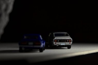 Mantova, İtalya - 3RD JANUARY 2025 Takara Tomy kopyaları gri Nissan Skyline 2000 GT-R ve mavi Nissan Fairlady Z beyaz bir panoda, gri bir kumaş parçasının yanında, uçurumun kenarındaki bir dağ yolunda yarış yapıyormuş gibi yapıyor.