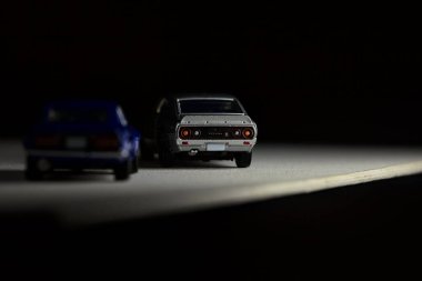 Mantova, İtalya - 3RD JANUARY 2025 Takara Tomy kopyaları gri Nissan Skyline 2000 GT-R ve mavi Nissan Fairlady Z beyaz bir panoda, gri bir kumaş parçasının yanında, uçurumun kenarındaki bir dağ yolunda yarış yapıyormuş gibi yapıyor.