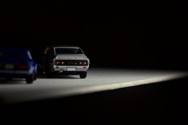 Mantova, İtalya - 3RD JANUARY 2025 Takara Tomy kopyaları gri Nissan Skyline 2000 GT-R ve mavi Nissan Fairlady Z beyaz bir panoda, gri bir kumaş parçasının yanında, uçurumun kenarındaki bir dağ yolunda yarış yapıyormuş gibi yapıyor.