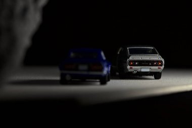 Mantova, İtalya - 3RD JANUARY 2025 Takara Tomy kopyaları gri Nissan Skyline 2000 GT-R ve mavi Nissan Fairlady Z beyaz bir panoda, gri bir kumaş parçasının yanında, uçurumun kenarındaki bir dağ yolunda yarış yapıyormuş gibi yapıyor.