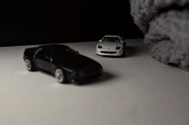 Mantova, İtalya - 3RD JANUARY 2025 - 1989 Mazda Savanna RX-7 'nin Ateşli Tekerlekleri ve Kibrit kutusu kopyaları ve beyaz bir tahtanın üzerinde beyaz bir kumaş parçasının yanında, uçurumun kenarındaki bir dağ yolunda yarış yapıyormuş gibi yapan Mitsubishi 3000 GT