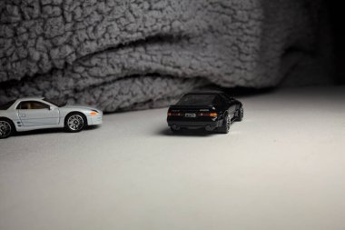 Mantova, İtalya - 3RD JANUARY 2025 - 1989 Mazda Savanna RX-7 'nin Ateşli Tekerlekleri ve Kibrit kutusu kopyaları ve beyaz bir tahtanın üzerinde beyaz bir kumaş parçasının yanında, uçurumun kenarındaki bir dağ yolunda yarış yapıyormuş gibi yapan Mitsubishi 3000 GT