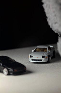 Mantova, İtalya - 3RD JANUARY 2025 - 1989 Mazda Savanna RX-7 'nin Ateşli Tekerlekleri ve Kibrit kutusu kopyaları ve beyaz bir tahtanın üzerinde beyaz bir kumaş parçasının yanında, uçurumun kenarındaki bir dağ yolunda yarış yapıyormuş gibi yapan Mitsubishi 3000 GT