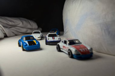 Mantova, İtalya - 4. JANUARY 2025 - çeşitli Porsche arabalarının Hot Wheels kopyaları, bir 911 rallisi, iki 1996 Carrera, bir 1971 911 ve bir 911 Carrera RS 2.7, beyaz tahta üzerinde, beyaz kumaşlarla çevrili, yolda bir eğri yapıyormuş gibi yaparak