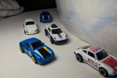 Mantova, İtalya - 4. JANUARY 2025 - çeşitli Porsche arabalarının Hot Wheels kopyaları, bir 911 rallisi, iki 1996 Carrera, bir 1971 911 ve bir 911 Carrera RS 2.7, beyaz tahta üzerinde, beyaz kumaşlarla çevrili, yolda bir eğri yapıyormuş gibi yaparak