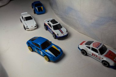 Mantova, İtalya - 4. JANUARY 2025 - çeşitli Porsche arabalarının Hot Wheels kopyaları, bir 911 rallisi, iki 1996 Carrera, bir 1971 911 ve bir 911 Carrera RS 2.7, beyaz tahta üzerinde, beyaz kumaşlarla çevrili, yolda bir eğri yapıyormuş gibi yaparak