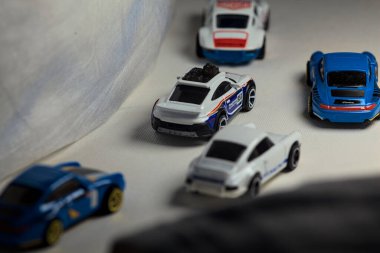 Mantova, İtalya - 4. JANUARY 2025 - çeşitli Porsche arabalarının Hot Wheels kopyaları, bir 911 rallisi, iki 1996 Carrera, bir 1971 911 ve bir 911 Carrera RS 2.7, beyaz tahta üzerinde, beyaz kumaşlarla çevrili, yolda bir eğri yapıyormuş gibi yaparak