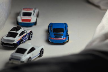 Mantova, İtalya - 4. JANUARY 2025 - çeşitli Porsche arabalarının Hot Wheels kopyaları, bir 911 rallisi, iki 1996 Carrera, bir 1971 911 ve bir 911 Carrera RS 2.7, beyaz tahta üzerinde, beyaz kumaşlarla çevrili, yolda bir eğri yapıyormuş gibi yaparak