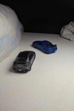 Mantova, İtalya - 4. JANUARY 2025 - Nissan Skyline GT-R V-Spec Nur II ve Mitsubishi Lancer Evolution 'ın beyaz panoda kopyaları, beyaz kumaşlarla çevrelenmiş, yolda bir eğri yapıyor ve aralarında bir yarış varmış gibi davranıyorlar.