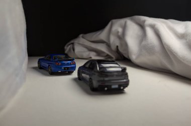 Mantova, İtalya - 4. JANUARY 2025 - Nissan Skyline GT-R V-Spec Nur II ve Mitsubishi Lancer Evolution 'ın beyaz panoda kopyaları, beyaz kumaşlarla çevrelenmiş, yolda bir eğri yapıyor ve aralarında bir yarış varmış gibi davranıyorlar.