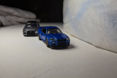 Mantova, İtalya - 4. JANUARY 2025 - Nissan Skyline GT-R V-Spec Nur II ve Mitsubishi Lancer Evolution 'ın beyaz panoda kopyaları, beyaz kumaşlarla çevrelenmiş, yolda bir eğri yapıyor ve aralarında bir yarış varmış gibi davranıyorlar.