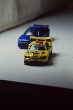 Mantova, İtalya - 10. JANUARY 2025 - Nissan Skyline GT-R V-Spec II Nur 'un Takara Tomy kopyaları ve 23. Pennzoil Nismo sarı renginde 1998 Nissan Skyline GT-R R33 ve bir devre eğrisi üzerinde yarış yapıyormuş gibi davranan siyah üniforma