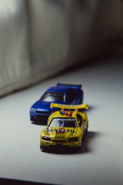 Mantova, İtalya - 10. JANUARY 2025 - Nissan Skyline GT-R V-Spec II Nur 'un Takara Tomy kopyaları ve 23. Pennzoil Nismo sarı renginde 1998 Nissan Skyline GT-R R33 ve bir devre eğrisi üzerinde yarış yapıyormuş gibi davranan siyah üniforma