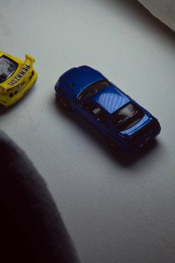 Mantova, İtalya - 10. JANUARY 2025 - Nissan Skyline GT-R V-Spec II Nur 'un Takara Tomy kopyaları ve 23. Pennzoil Nismo sarı renginde 1998 Nissan Skyline GT-R R33 ve bir devre eğrisi üzerinde yarış yapıyormuş gibi davranan siyah üniforma