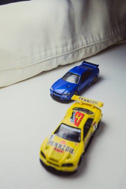 Mantova, İtalya - 10. JANUARY 2025 - Nissan Skyline GT-R V-Spec II Nur 'un Takara Tomy kopyaları ve 23. Pennzoil Nismo sarı renginde 1998 Nissan Skyline GT-R R33 ve bir devre eğrisi üzerinde yarış yapıyormuş gibi davranan siyah üniforma