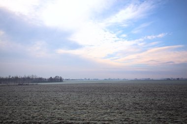 Üzerinde seyrek ağaçlar bulunan, kıpır kıpır tarlalarla kaplı, bir ev silueti ve bir köy kilisesi olan, İtalya 'nın kırsal kesimlerinde bulutlu bir günde