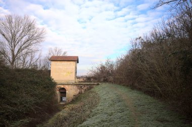 Bir barajın üzerinde terk edilmiş eski bir bina, bir parkın ortasında, izlerle kaplı boş bir hendeğin yanında, İtalya 'nın kırsal kesimlerinde bulutlu bir günde