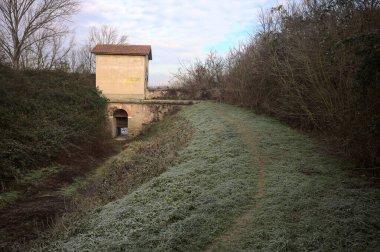 Bir barajın üzerinde terk edilmiş eski bir bina, bir parkın ortasında, izlerle kaplı boş bir hendeğin yanında, İtalya 'nın kırsal kesimlerinde bulutlu bir günde