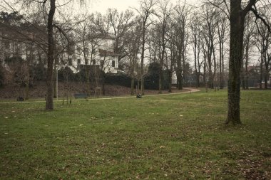 Kışın bulutlu bir günde, İtalya 'nın bir kasabasında ağaçlarla çevrili bir binanın yanındaki kavak ağaçlarıyla çevrili bir patikaya tırmanmak.