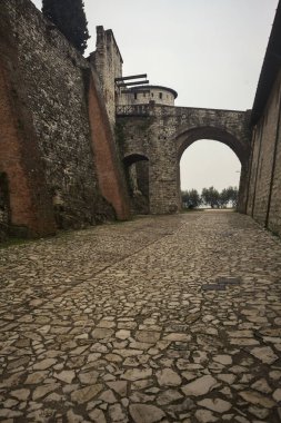 Bulutlu bir günde, bir şatonun taş duvarları arasında, ucunda bir köprü olan bir bahçe.